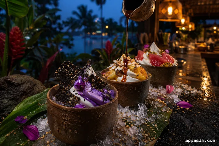 Three elaborate tropical frozen yogurt desserts with purple yam, roasted pineapple, guava, sesame brittle, toasted grains, passion-fruit pearls, and flowing palm syrup at a rain-wet blue-hour counter.