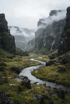 Portrait fine art landscape of a misty basalt valley with a winding silver river, wet grasses, dark volcanic cliffs, and low morning cloud.