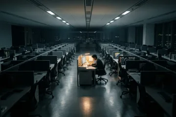 Lone office worker at one illuminated desk surrounded by rows of dark empty cubicles in a cinematic late-night workplace.