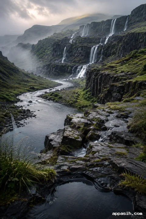 Elevated portrait view across wet basalt slabs toward layered waterfalls, a winding reflective river, mossy terraces, and mist-covered highlands after rainfall.